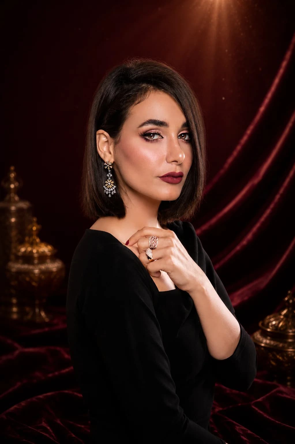 Model wearing earrings, a layered necklace, and rings against a maroon velvet backdrop